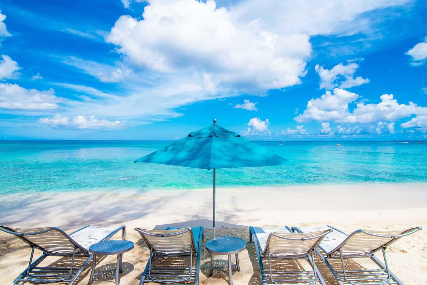 Turquoise Cayman Islands beach with a blue umbrella and loungers, representing the Cayman Islands company search service