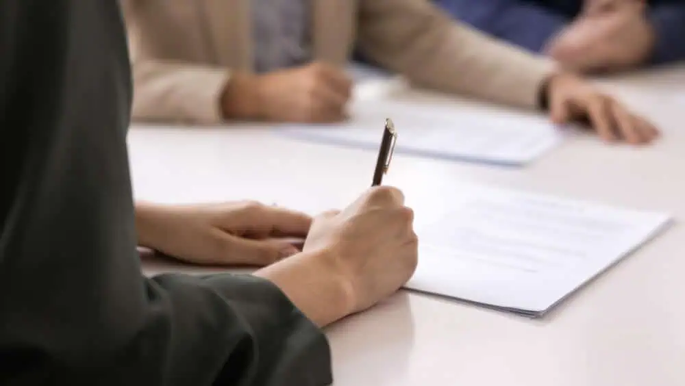 Three people at a conference table signing constitutional documents for a private trust company.