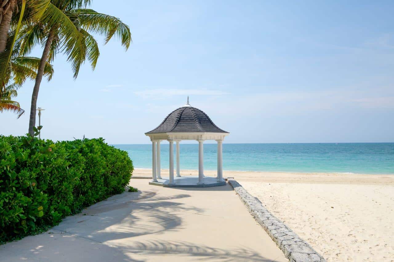 White gazebo at the end of a palm-lined beach walkway overlooking turquoise water in The Bahamas