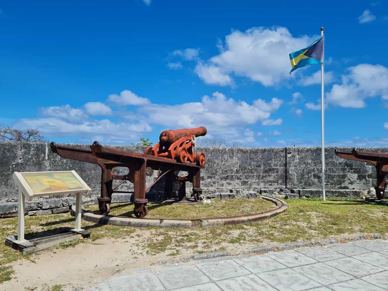 Bahamian flag flying over a historic iron cannon and limestone wall at a fort in The Bahamas