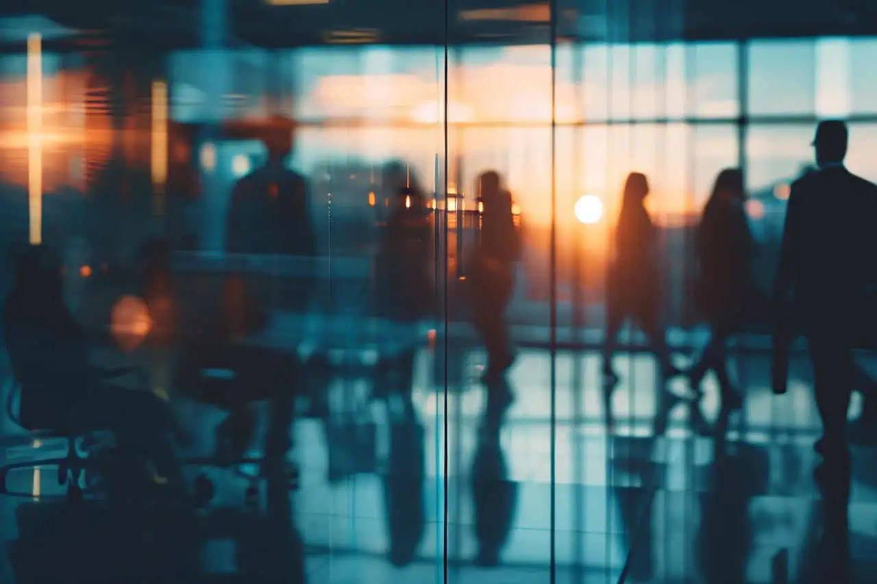 Silhouettes of business professionals behind a glass office partition at sunset, seen through reflected light