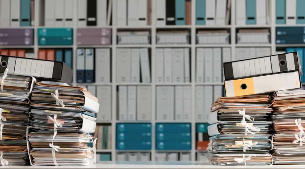 Corporate records and ring binders stacked in front of an archive shelf, of the kind a registered agent maintains