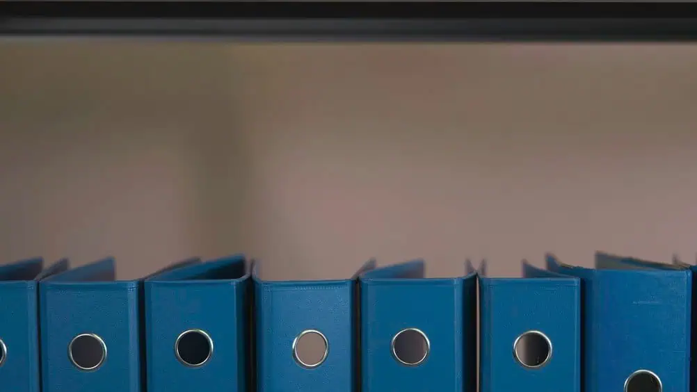 Row of identical dark blue ring binders standing on a shelf, illustrating shelf companies held in stock until a buyer needs one